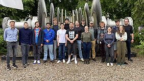 Mehrere Personen stehen vor einer großen Turbine mit vielen Laufrädern an der Welle.