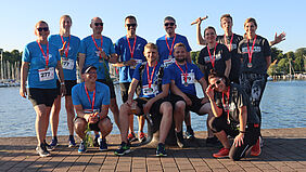 es sind 12 Läuferinnen und Läufer mit ihren Medallien an der Kaikante im Rostocker Stadthafen zu sehen.