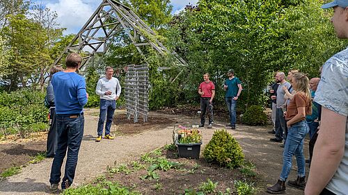 Hochschulangehörige stehen in einem Garten im Kreis um Prof. Hillmann herum, der eine Rede hält.