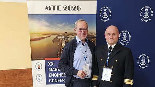 Zwei Männer mit Namensschildern stehen vor Bannern der MTE 2026 und der Politechnika Szczecińska