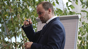 Mathias Lorenz hält einen Stift in der Hand und steht vor einem Flipchart. Er gestikuliert in Richtung Publikum.