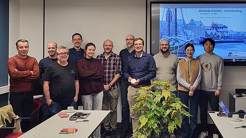 11 Personen stehen nebeneinander in einem Beratungsraum. Im Hintergrund ist eine Präsentation zu sehen.