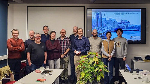 11 Personen stehen nebeneinander in einem BEratungsraum. Im Hintergrund ist eine PRäsentation zu sehen.