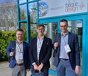 Prof. Dr.-Ing. Ralf Glienke steht mit zwei Kollegen vom Fraunhofer IGP vor dem Eingang zur 11. Internationalen Fatigue-Design-Konferenz in Frankreich