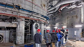 Mehrere Personen mit Schutzhelmen laufen entlang einer großtechnischen Industrieanlage.