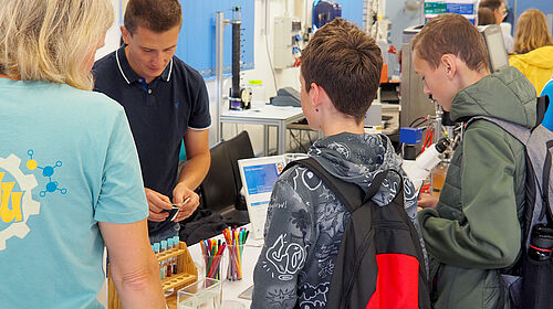Mitarbeiter Kevin Bläsing (2.v.l.) zeigt zwei Schülern in einem Labor die Wirkungsweise der Chromatografie.